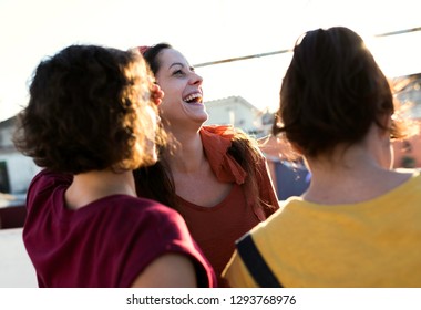 Crop Back View Of Brunette Women In Bright Summer Casual Clothes Standing On Roof Terrace And Happily Laughing On Sunny Summer Day On Blurred Background