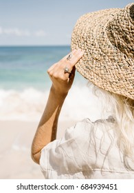 Crop back view of woman touching straw hat on background of ocean. 