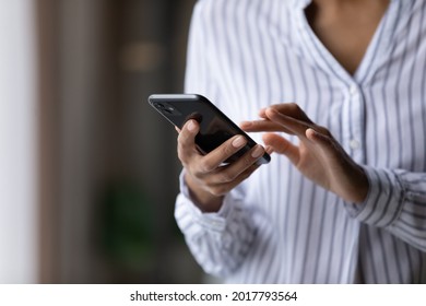 Crop close up of African American woman hold cellphone text message online on gadget. Ethnic biracial female use smartphone browse surf wireless internet on device. Technology, communication concept.