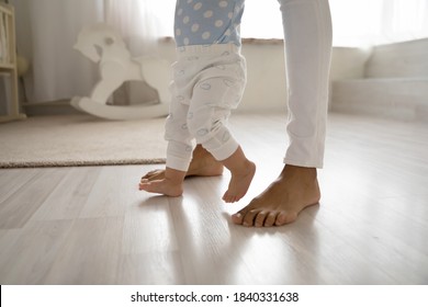 Crop Close Up Of Biracial Little Toddler Infant Make First Steps On Home Floor Hold Loving Mother Hands. Small African American Baby Child Learn Walking With Mom Support Care. Childcare Concept.