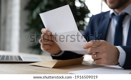 Crop close up businessman sit at desk reading post paper letter or correspondence in office. Male employee or director receive consider postal paperwork or mail notification at workplace.