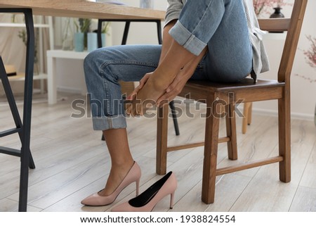 Crop close up of businesswoman sit at desk in office take off uncomfortable heels shoes suffer from legs pain ache. Female employee touch massage feet, feel discomfort in foot, have strained muscles. 商業照片 © 