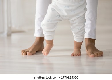 Crop close up of caring African American mom hold small toddler daughter hands make first steps together. Little baby kid child learn walking on wooden floor in home with mother. Childhood concept. - Powered by Shutterstock