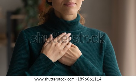 Crop close up of Caucasian woman hold hands in prayer at heart chest feel religious superstitious. Young female believer being grateful thankful pray to God. Faith, belief, religion concept.