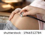 Crop close up of doctor hold stethoscope listen to pregnant woman baby bump, check kid in womb. Nurse or gynecologist use phonendoscope examine child in belly heartbeat. Pregnancy concept.