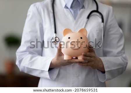Crop close up female doctor physician nurse wearing white uniform with stethoscope holding pink piggy bank, medical insurance concept, healthcare and medicine, hospital budget, clinic fees