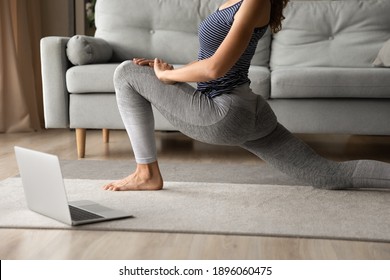 Crop close up of fit sporty woman in sportswear stretching at home training online using computer. Active young female do morning gymnastics practice yoga on webcam class or distant lesson on laptop.