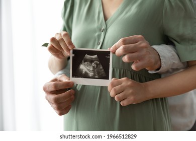 Crop close up of happy young multiethnic future parents hold ultrasound picture of baby. Diverse man and pregnant woman show sonogram image on kid child, excited for parenthood. Parenting concept. - Shutterstock ID 1966512829