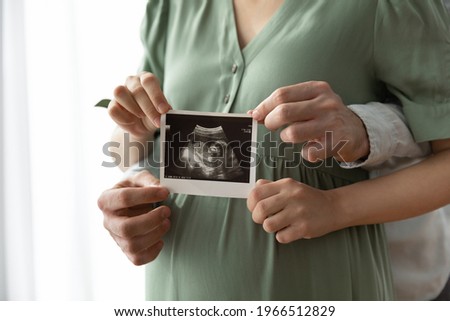 Crop close up of happy young multiethnic future parents hold ultrasound picture of baby. Diverse man and pregnant woman show sonogram image on kid child, excited for parenthood. Parenting concept.