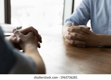 Crop close up of male business partners sit at desk with hands clasped talk at meeting in office. Businessmen or opponents face each other at business negotiation at workplace. Rivalry concept.
