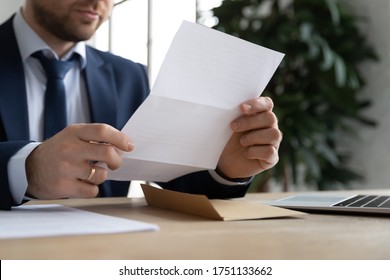 Crop close up of male employer sit at office desk hold paperwork correspondence analyzing report or statistics, Caucasian businessman read consider postal paper document or post letter at workplace - Shutterstock ID 1751133662