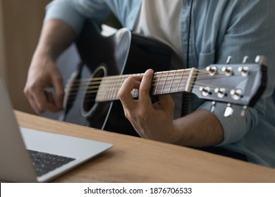 Crop close up of male music coach or tutor play guitar have online video lesson on laptop at home studio. Man artist or singer use musical instrument record new song or single. Hobby concept. - Powered by Shutterstock