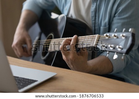 Crop close up of male music coach or tutor play guitar have online video lesson on laptop at home studio. Man artist or singer use musical instrument record new song or single. Hobby concept.