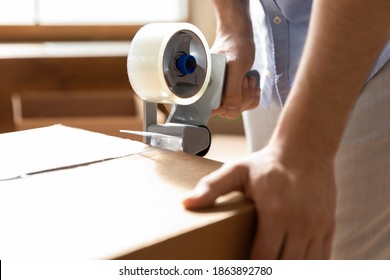 Crop close up of man close pack box with personal belongings using tape dispenser. Male renter or tenant wrap package with adhesive scotch, moving relocating to new house home. Realty concept. - Shutterstock ID 1863892780