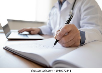 Crop close up of middle-aged male doctor write in medical journal fill patient information use laptop online. Mature man GP or therapist make notes work distant on computer in clinic or hospital. - Powered by Shutterstock