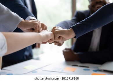 Crop close up of multiracial businesspeople give fists bump participate in teambuilding activity at meeting. Motivated diverse colleagues join hands take part in training, show motivation for success.