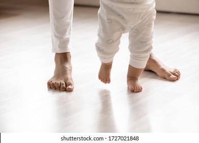 Crop Close Up Of Small Biracial Toddler Infant Make First Steps On Home Wooden Floor Holding Mom Hands, Little African American Baby Child Learn Walking With Mother Support Care, Childcare Concept