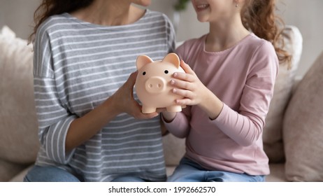 Crop Close Up Of Smiling Hispanic Mom And Biracial Daughter Hold Piggy Bank Recommend Family Savings. Happy Latin Ethnic Mother And Teen Girl Child Use Piggybank Care Of Budget For Money Investment.