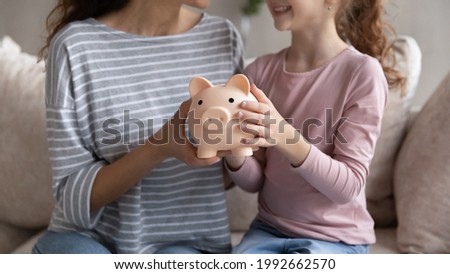 Crop close up of smiling Hispanic mom and biracial daughter hold piggy bank recommend family savings. Happy Latin ethnic mother and teen girl child use piggybank care of budget for money investment.