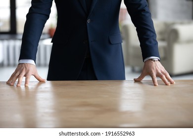 Crop close up of successful businessman in suit stand near table in office show power and confidence in business relations. Determined male CEO or director at workplace. Leadership, success concept.