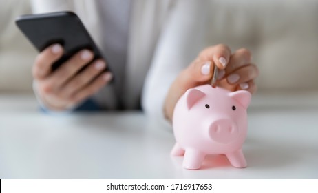 Crop close up of woman put coin in piggy bank save money for future, use financial app on cellphone, female or housewife manage household finances or expenditures, account investment on smartphone