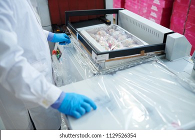 Crop confectionery factory worker using sealing machine to pack paper box with pastry into plastic film.