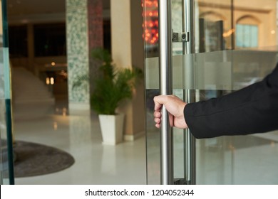 Crop Doorman In Black Suit Opening Glass Doorway Of Hotel Welcoming Guests