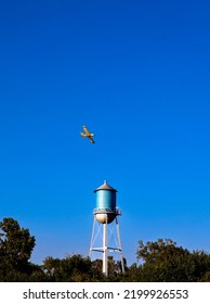 Crop Duster Over Small Town Water Tower