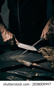 Crop faceless male chef sharpening metal blade of knife with sharpener while working in dark kitchen