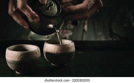 Crop Faceless Person Pouring Hot Drink From Old Fashioned Metal Teapot Into Cup On Table During Tea Ceremony In Kitchen