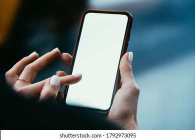 Crop Faceless Young Stylish Female Browsing Mobile Phone With White Empty Screen Tapping With Finger On Display Standing On Blurred Street Background