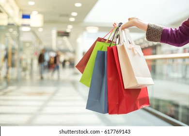Crop female hand holding colorful paper bags on background of shopping center. - Shutterstock ID 617769143