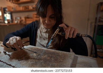 Crop female master with gas burner creating metal piece of handmade accessory in handicraft workshop - Powered by Shutterstock