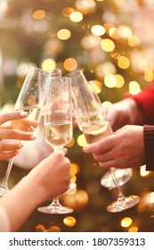 Crop hands of faceless men and women clinking glasses of champagne with beautiful green Christmas tree on blurred background