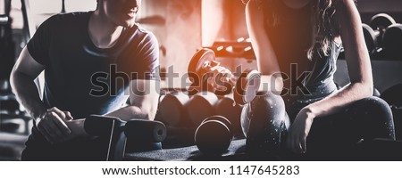 Crop image of beautiful sport girl with dumbbell in hand with personal trainer in professional gym, color filter effect selective focus.