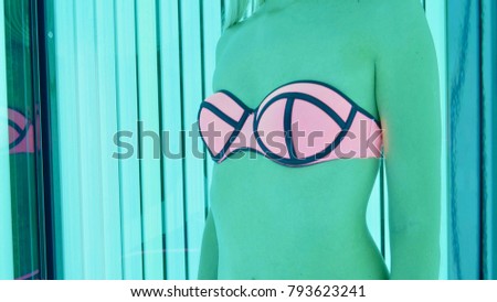 Crop image body of woman in pink and blue swimsuit standing in tanning booth. Concept of spa treatments and beauty center.
