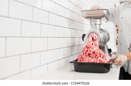 Crop of incognito woman with curly hair putting small pieces in meat grinder and grinds them into mincemeat. View of female working in butchery, preparing meat for selling in shop. - Powered by Shutterstock