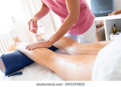 Crop masseuse rubbing skin of female client leg with oily spray in clinic - Powered by Shutterstock