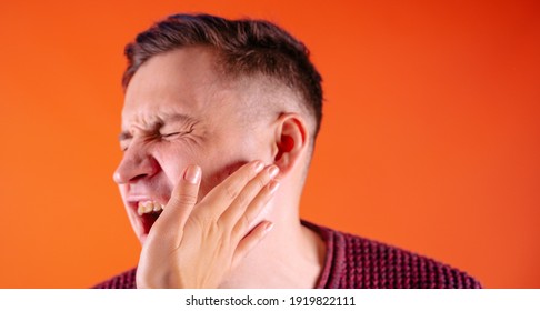Crop person slapping scared man in face. Emotional male getting slapped in face while shouting with closed eyes in fear on orange background.