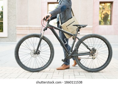 Crop Photo Of An Active Businessman Carrying A Messenger Bag And Walking His Bike To The Office. Man Using An Eco-friendly Vehicle To Commute To Work 