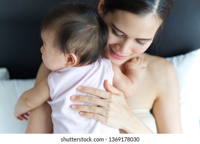 Crop Shot Of Beautiful Asian Mother Holding Baby's Back On The Bed. Seen From Behind The Baby. Mother Is Feeling Love And Smiling To Her Kid. Love And Relation Bond Of Mother And Child Concept.