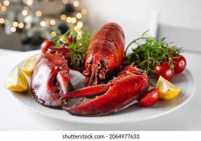 Crop Shot Of Freshly Cooked Red Lobster With Vegetables On A Plate And White Table. Christmas Light On A Background. Holidays Food Concept