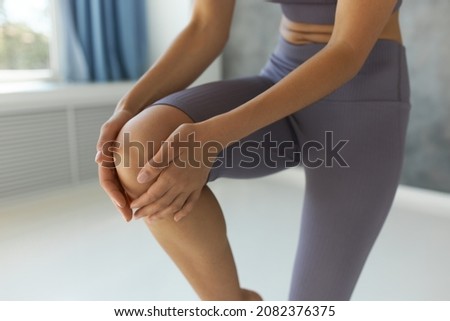 Crop shot of random Caucasian woman doing yoga in lilac crop top and leggings, touching gently right knee, balancing on left foot, having cute abdominal folds, isolated over fitness studio background