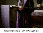 Crop shot of unrecognizable senior Catholic priest wearing soutane and stole standing indoors reading Bible