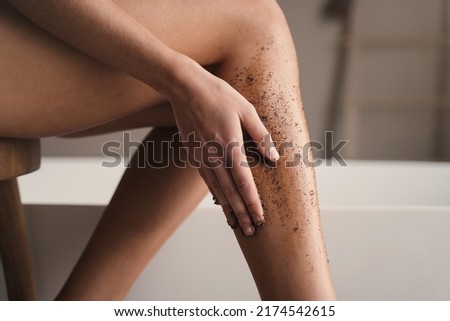 Crop shot of woman hand scrubbing legs with organic scrub in bathroom during anti-cellulite massage. Body and skin care. peeling and exfoliating procedure