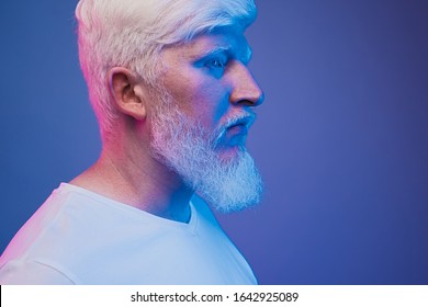 Crop Side View Of Serious Albino Man With Bear Wearing White T Shirt Looking Away In Glowing Blue Neon Light