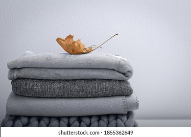 Crop stack gray woolen knitted blankets   warm plaids decorated maple leaf  autumn cozy concept