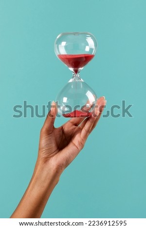 Crop unrecognizable African American female showing hourglass with red sand against turquoise background