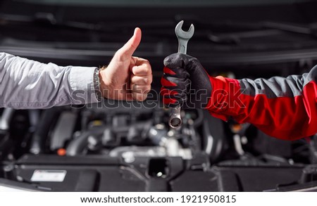Crop unrecognizable businessman showing thumb up gesture while standing with auto mechanic with wrench in hand near broken car in garage