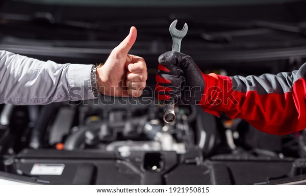 Crop unrecognizable businessman showing thumb up\
gesture while standing with auto mechanic with wrench in hand near\
broken car in garage
